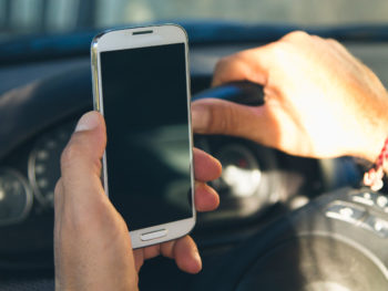Man driving in a car distracted by a smart phone in hand